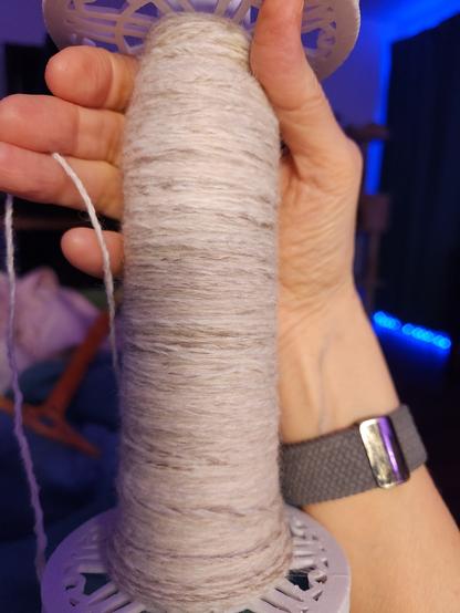 My hand holding a bobbin of pale beige yarn.