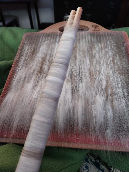 The blending board loaded up with wool, rabbit fur, and mohair fiber, ready to be rolled off into rolags. One freshly made rolag is shown still on two rolling sticks.