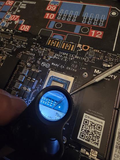 A laptop motherboard with a Jeweler's lens hovering over it as I inspect the CPU for liquid metal