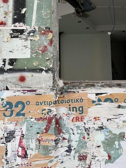 Colour photograph: a construction site. The shell of a building on Solonos St in Exarcheia. A window opening into a square bare white interior. Layers of posters have been peeled off the wall making a pale, torn, multicoloured surface, green and white and beige. Most torn remnants are illegible but one advertised the 32nd anti-racist something to do with maybe camping - my guess is a music festival