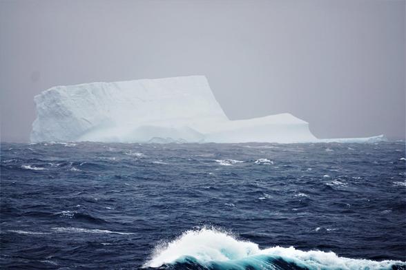 photo of a large iceberg in a stormy polar ocean