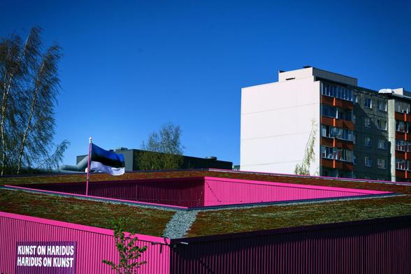 Lasnamäen paviljonki, jonka kyljessä slogan ”kunst on haridus, haridus on kunst”. Paviljongin sisäpihalta pilkottaa Viron lippu salossa. Taustalla puita ja kerrostalo, pari.