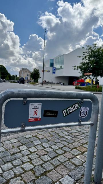 Sticker on the back of a road sign representing a cartoonish hand linked to foot by a black limb and is ticking the foot with a feather. The text on the sticker says «  The Vicious Cycle » by NoeGrit