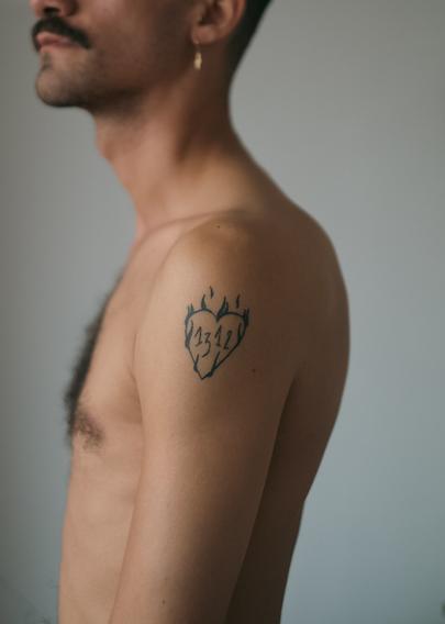 Self-portrait in profile, cropped just above my mustache. On my shoulder is a tattoo of a burning heart with the numbers 1312