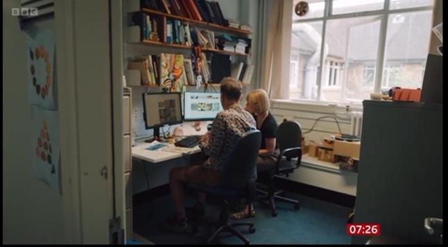 Angus Davison in messy office with Vic Gill, both looking at computer