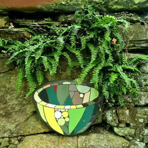 An image of a small bowl made from a mosaic of tiles on an old wall in a Glasgow Park.