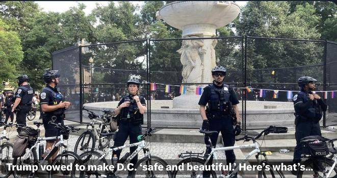 A group of police officers in uniforms and helmets stands near a fountain surrounded by a fence. Bicycles are parked in the foreground, and colorful flags are visible in the background. The scene suggests a public gathering or event.