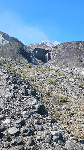 Looking up a rocky mountainside at spectacular huge waterfalls. Two streams of water fall over an edge and strike a rock and turn into huge spraying cascades.