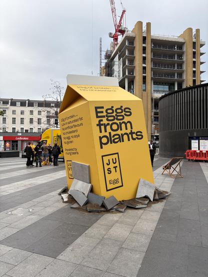Giant ‘Eggs from plant’ yellow carton about 2m tall placed on surface at angle to make it look like it is smashing up paving tiles.