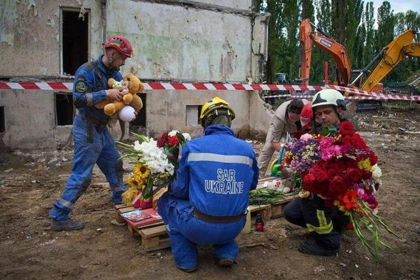 Rescuers lay toys and flowers on the site of Russia's Thursday night missile strike that hit a multistory residential house killing 31 civilians including five children in Kyiv