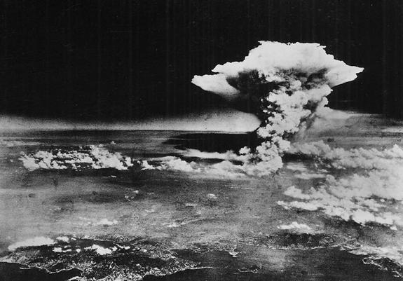 Imagen aérea en escala de grises de la bomba atómica lanzada por Estados Unidos contra Hiroshima, Japón. Se ve la costa, más cercana, la ciudad con una ligera bruma, nubes por debajo de la altitud a la que volaba el bombardero, y la columna de humo en forma más o menos de hongo, más desdibujado que la típicas de experimentos posteriores. El cielo se ve muy oscuro, sorprendentemente, supongo que porque desde tan alto, el azul es bastante oscuro y la película en blanco y negro apenas lo registraría.