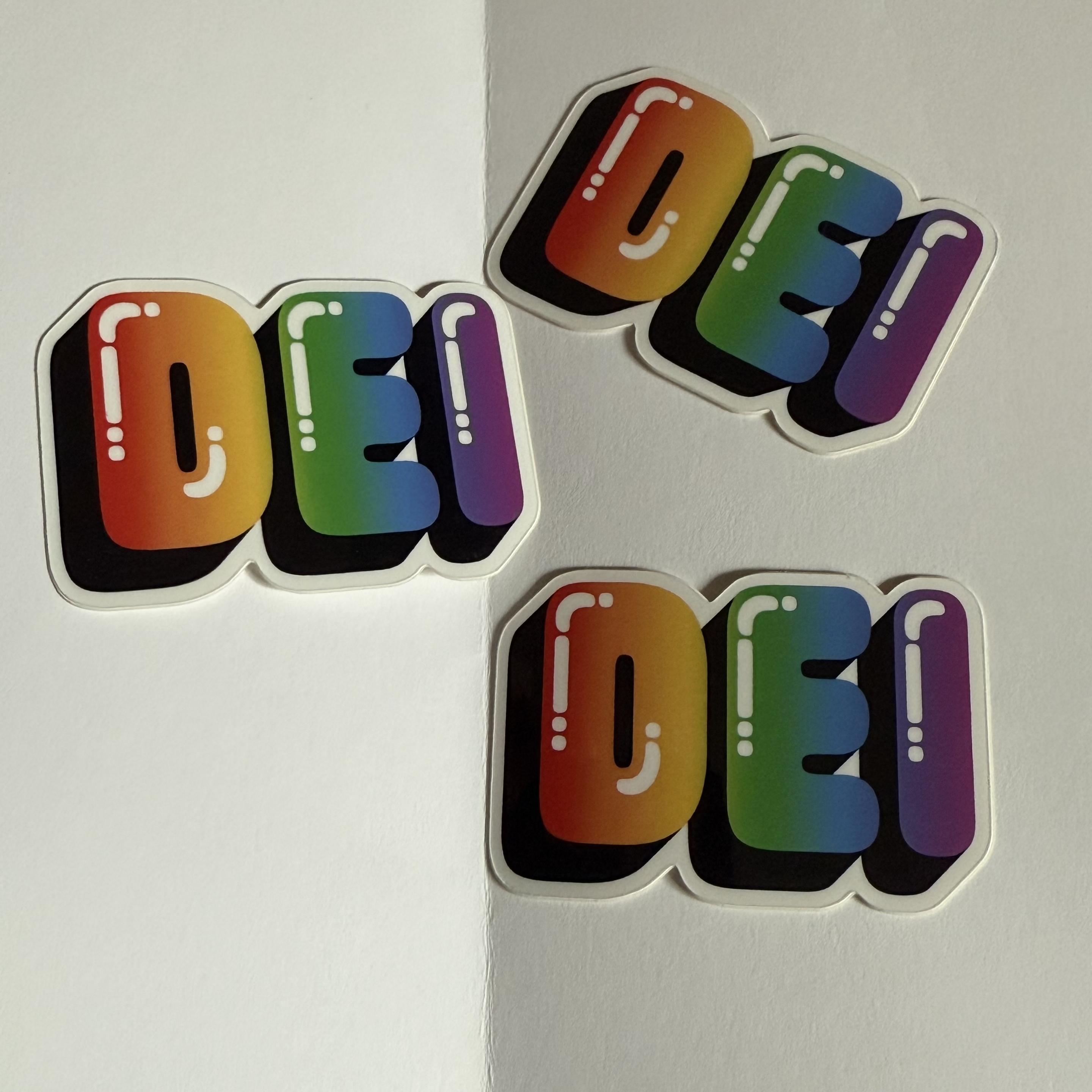 Three colourful stickers of the text “DEI” in a rainbow bubble font.
