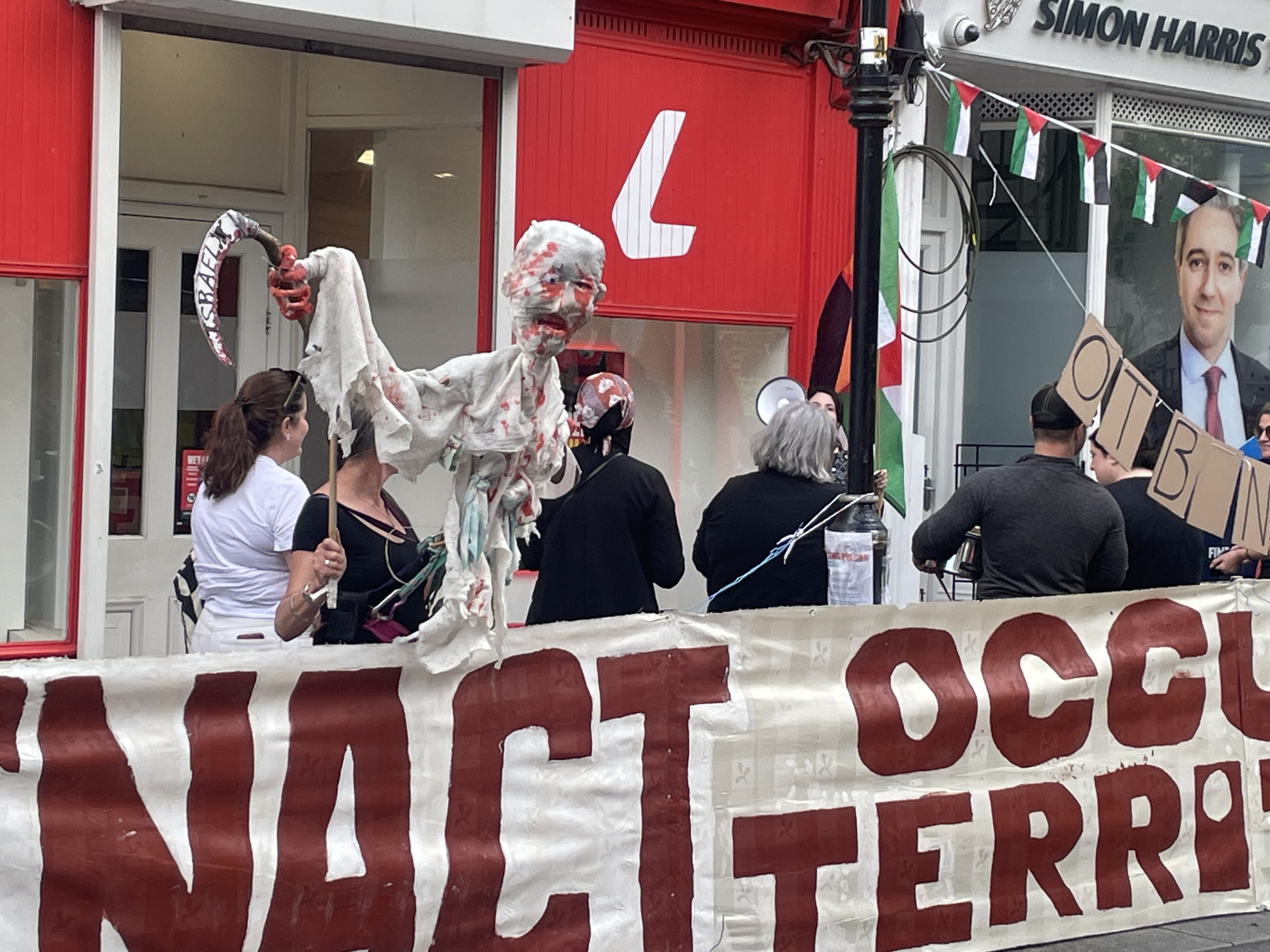 Protestors in front of Simon Harris’s office in Bray, Ireland. Israel is depicted as a bloodied grim reaper.