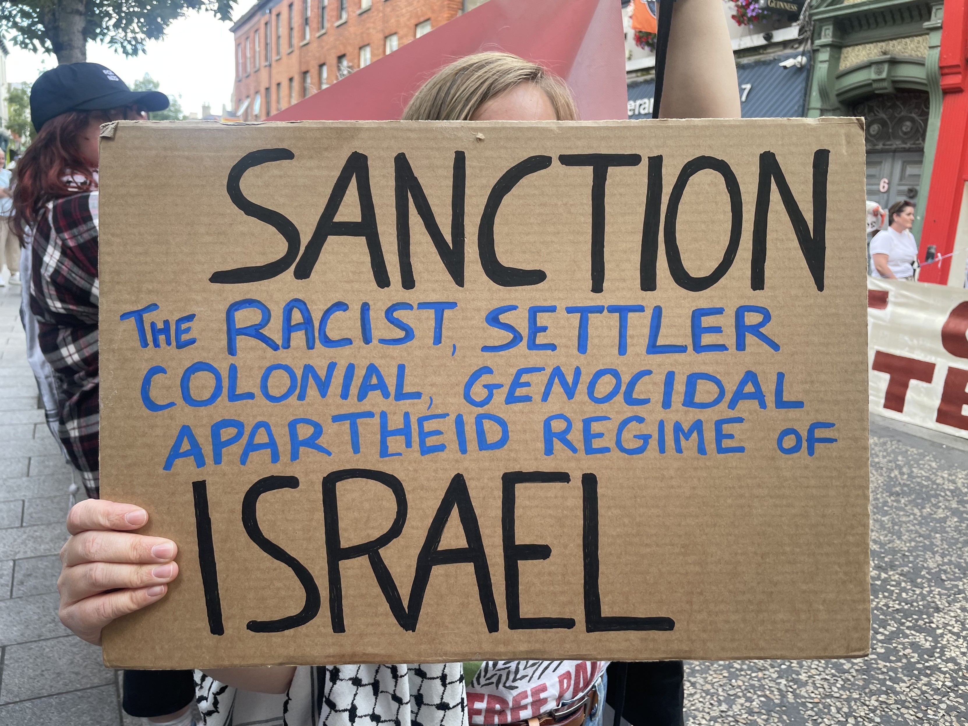 Protester holding sign: “Sanction the racist settler colonial genocidal apartheid regime of Israel.”