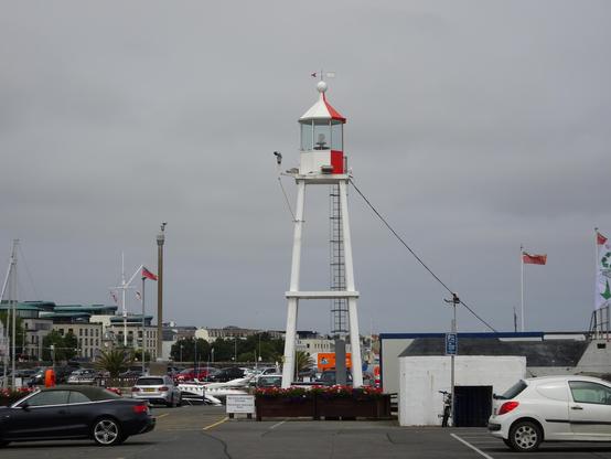 White lighthouse in the St Peter Port Marina in front of a cloudy grey sky.
