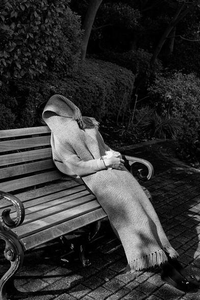 A young woman, covered with her wrap, takes a nap on a bench outside during her lunch break.