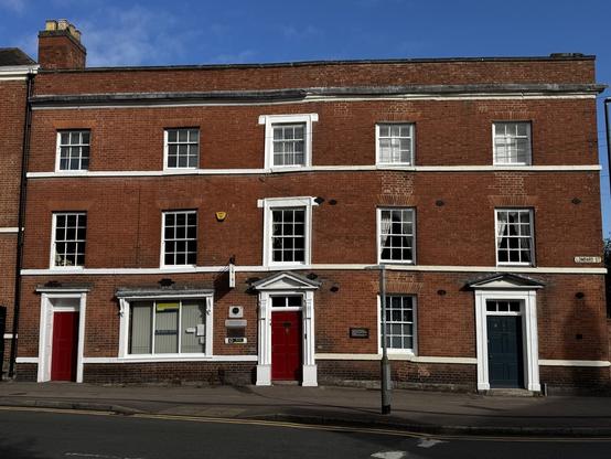 Georgian brick building with three stories, three red front doors and a range of multi planed windows