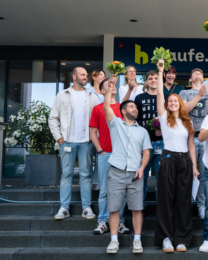 Gruppenfoto, Gruppe (linke Seite) steht auf einer Treppe vor dem Haufe Group Eingang und wirft Blumensträuße nach oben.