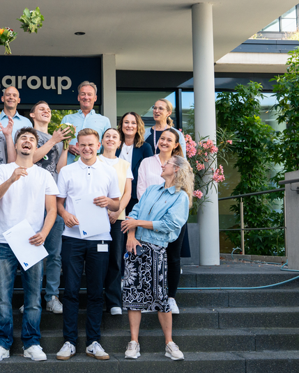 Gruppenfoto, Gruppe (rechte Seite) steht auf einer Treppe vor dem Haufe Group Eingang und wirft Blumensträuße nach oben.