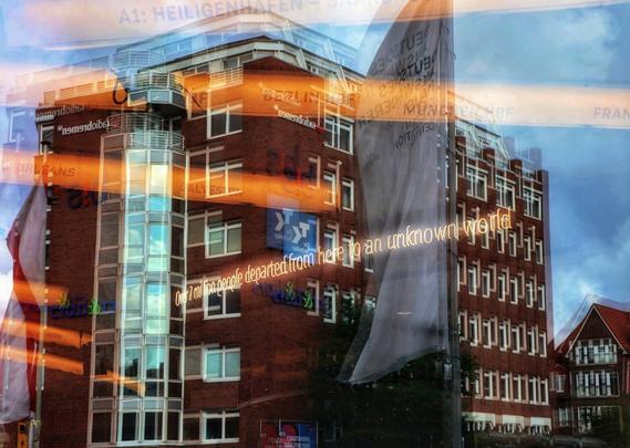 A photograph taken from outside the German Emigration Center museum (Deutsches Auswandererhaus) in Bremerhaven, looking in through a large window. The reflections of a large, modern brick building with numerous windows and a rounded glass section as well as another building and flags are visible on the glass. Inside the museum, an exhibition is displayed behind the window, featuring white neon writing with the phrase "Over 7 million people departed from here to an unknown world" on it. The neon writing and the buildings are superimposed in the reflection. Bright orange and white light streaks, likely from a display inside the museum, and the text "A1: HEILIGENHAFEN" as well as "BERLIN" and "MÜNCHEN", amongst others, likely departure cities for German emigrants, are also part of the interior exhibition, appearing as a dynamic overlay on the static reflection of the external buildings. The image is a complex blend of interior exhibition elements and exterior reflections.