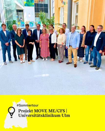 Eine Gruppe von 16 Personen steht in einem hellen Foyer des Universitätsklinikums Ulm, darunter Minister Manne Lucha sowie Mitarbeitende der Uniklinik Ulm. Text: Projekt MOVE ME/CFS,  Universitätsklinikum Ulm.