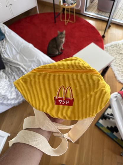 Un sac banane en velours jaune avec une sangle couleur blanc cassé. Le logo McDonald’s est brodé, avec des symboles asiatiques, peut-être bien japonais, dans le rectangle rouge sous le M jaune.