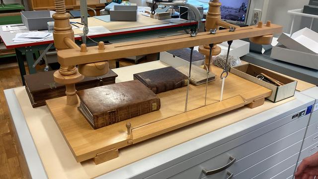 Book frame made of light wood lying on a white metal chest of drawers, with two books on top and one next to it on the top left.