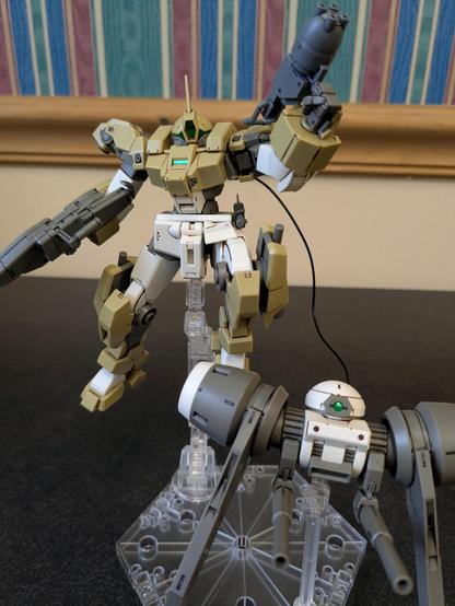 The HG Demi Barding with its backback drone. Both are on a stand. The Demi Barding is holding a rifle in one hand and the multi cannon from the Daedalus system in the other.