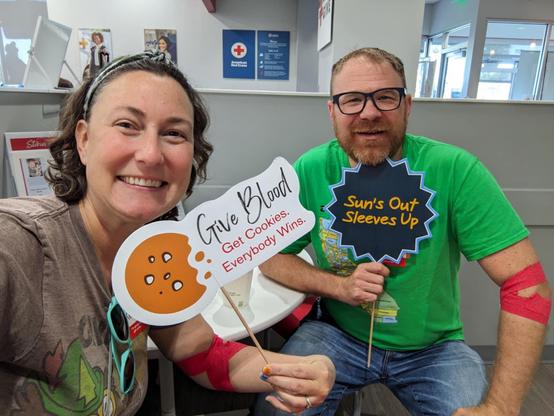 Man in green shirt holds a sign saying suns out sleeves up and a woman holds the cookie sign