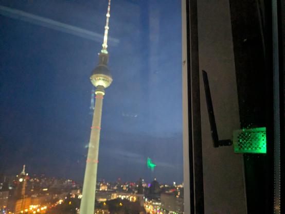Mein TTN-Reisegateway ist im gekippten Hotelzimmerfenster eingeklemmt, eine grüne LED blinkt bei jedem Datenpaket.
Im Hintergrund sind die Dächer von Berlin (aus dem 22. Stock) und der Fernsehturm zu sehen.