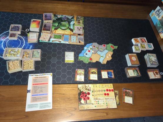A wooden table seen from above. The table is occupied by a solo game of Spirit Island in its end state. The Spirit is Keeper of the Forbidden Wilds. Very few Invaders nor Dahan remain, and all of the Spirit's Powers have been played this turn. Just this turn, Terror Level II has been achieved, winning the game as there are no more Cities nor Towns on the Island.

The various token supplies sit around the table in custom cardboard tray / boxes. To the left is a Turn Phase reference sheet.