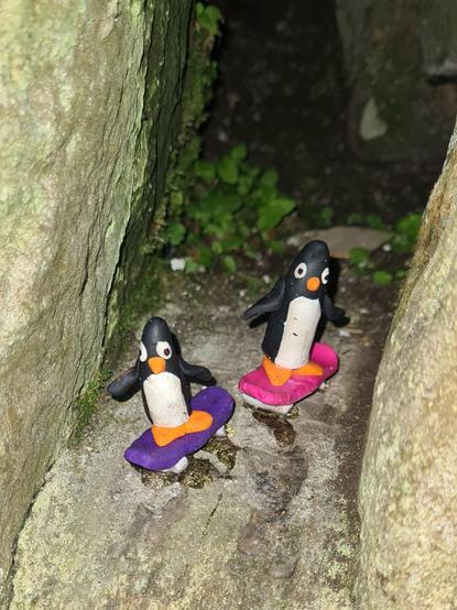 A pair of small model penguins on skateboards.