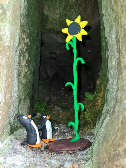 Two small model pengiuns looking up at a massive sunflower which is towering over them.