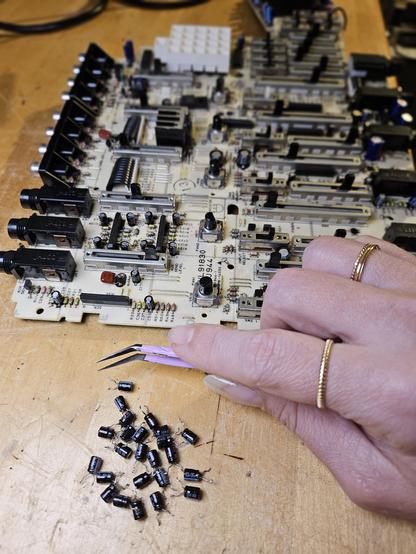 Background object is a PCB and internal workings of a vintage 4-track Yamaha cassette tape recording device. Foreground is my hand, holding angle-grip, very pointy tweezers over a pile of old, worn out capacitors I removed and replaced with new, compatible capacitors.