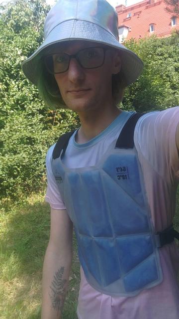 Takie barto na dworze robi sobie selfi. Ma kamizelke chłodzącą niebieską.