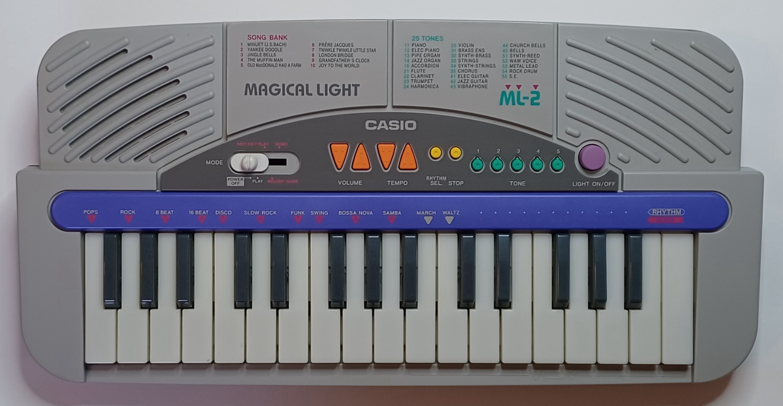 The Casio "Magical Light" ML-2 keyboard, in a cool gray color with a vivid deep indigo bar along the top of the keys, and a darker gray panel with other buttons in orange, yellow, green, and purple.