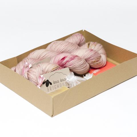 Picture shows an open A4 box containing two skeins of yarn in shades of pink with raspberry and ginger speckles. The rest of the contents is obscured by the sides of the box.