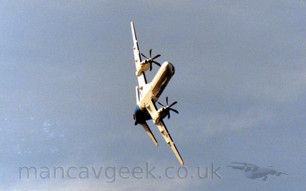 Low shot of a twin propellor-engined airliner banking hard as it flies from left to right during a display flight.
The plane is mostly white, with a blue tail, the sun coming from the left of the frame blowing a lot of details on that side while leaving the far side dark.
Blue sky fills the rest of the frame.