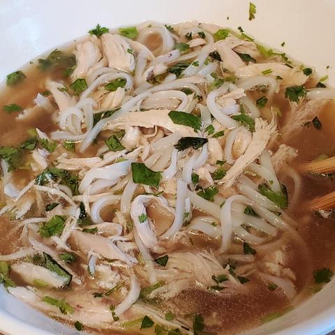 Bowl of chicken pho soup, featuring shredded chicken, rice noodles, fresh basil and cilantro, and a clear, flavorful broth.