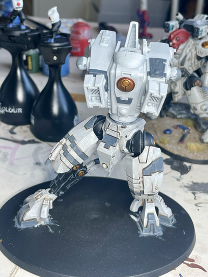 Front view of t’au riptide battlesuit in process of being built and painted. Legs are fully painted, but the torso only has base paints and now arms or head has been attached.