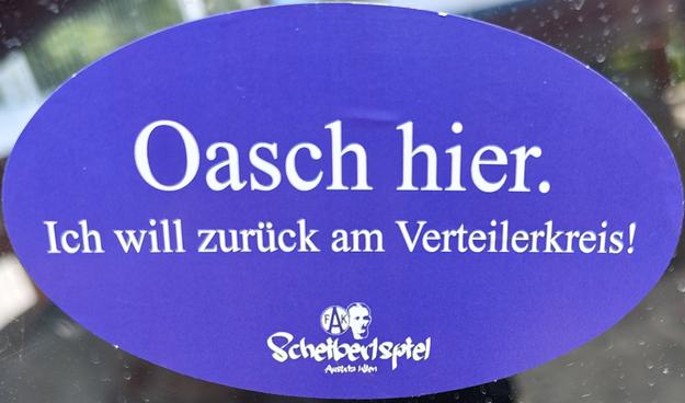 Ein Aufkleber des Austria Wien-Fanclubs Scheiberlspiel, auf dem steht „Oasch hier. Ich will zurück am Verteilerkreis.“