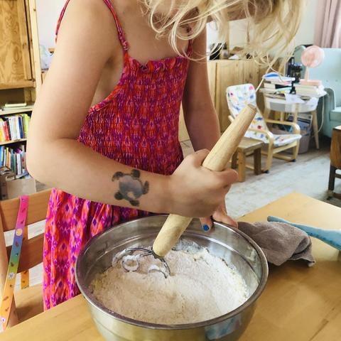 A white 5 year old girl with shoulder length blonde hair wearing a bright pink spaghetti strap dress, stirring in a stainless steel bowl to mix the pie crust ingredients. She is looking down at the bowl, her face obscured by her hair. We don’t show her face on social media for privacy reasons, at least until she’s at an age where she can understand the risks and consent to it.