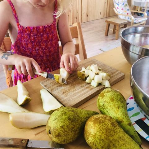 Same girl cutting up pears with a sharp peeling knife on a wooden cutting board