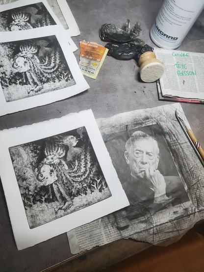 Photo : même que précédente, mais la plaque n'est plus là et révèle le papier journal en dessous : la tête d'un type âgé à l'air sévère qui se tient le menton d'un air dubitatif en regardant en direction d'un des tirages.
On voit un autre papier journal d'emballage de la plaque de cuivre, sur lequel est écrit au stylo CUIVRE TETE POISSON