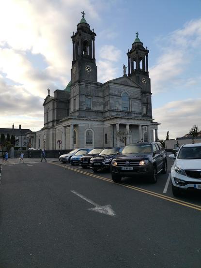 Église d'Athlone, vue de 3/4. Édifice en pierre gris clair, à fronton et deux clochers.