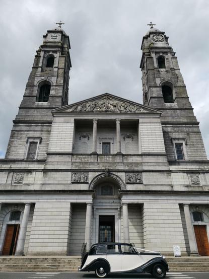 Église de Mullingar : façade à serlienne et portique à fronton superposés. Deux clochers à base carrée. Une voiture de collection des années 30 est stationnée devant.