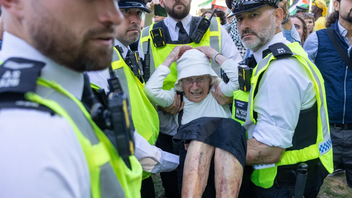 three cops carrying an elderly woman wearing a white hat.