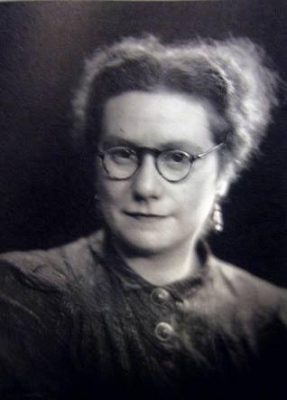 Vintage black-and-white portrait of a woman wearing glasses and a high-collared blouse, exuding a formal and reflective atmosphere.