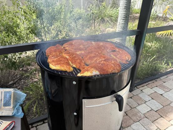 Action shot of a bunch of boneless skinless dry-rubbed chicken breasts on a 22-inch Weber Smokey Mountain grill.