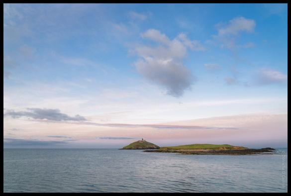 Ballycotton Lighthouse standing on a small green island surrounded by calm waters under a pastel evening sky with soft clouds after sunset, County Cork.